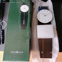 Clock next to original green Howard Miller box showing model name and full view of clock protected by foam.