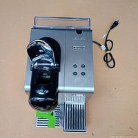 Top view of DeLonghi Nespresso machine showing chrome lever, control buttons, drip tray and power cord