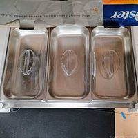 Open box showing three stainless pans with lids inside base