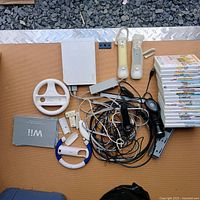 Full lot view with console, controllers, cables, wheels, manual and game stack