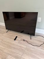 Front view of Samsung 43" TV on stand with remote and power cord visible