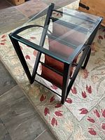 Side view of table showing glass top, black frame, magazine rack