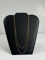 Two gold chains displayed on black bust, shorter inside longer