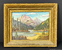 Full view of framed acrylic landscape painting showing mountain, lake and forest scene with visible signature M. Woods in the lower right.