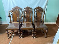 Full view of five matching armless antique wooden dining chairs with carved backs and turned legs.