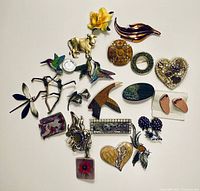 Full view of 20 assorted brooches in wood and metal materials of various designs including animals, flowers, abstract shapes, and figurative forms