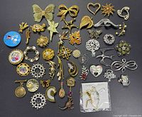All brooches laid out on a flat dark surface showing full collection including silver, gold, ceramic and fabric designs