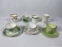 Overall view of all eight assorted china and porcelain cups and saucers including floral, green, and souvenir styles