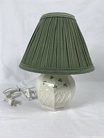 Full view of Belleek ceramic lamp with green fabric shade, showing shamrock decoration and electrical cord with plug.