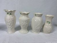 Four Belleek porcelain vases arranged in a row with varying heights and shamrock designs visible