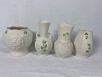 Front view of Belleek mini cache pot and three small vases arranged side by side showing embossed Celtic patterns and green shamrocks.