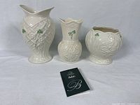 Photo of two Belleek vases and one Celtic style cache pot with shamrock and floral details displayed on white surface