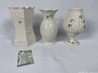 Front view of three Belleek ceramic pieces: Kilkenny Castle vase, Lindisfarne vase, and fairy lamp with shamrock decorations.