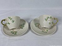 Pair of Belleek teacups and matching saucers with shamrock and gold accents shown side by side on white background.