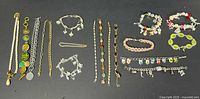 Photo shows assortment of 11 bracelets including charm bracelets, chain link, beaded and faux pearl designs spread out on a black background.