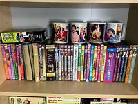 Shelf showing various British TV series DVDs including Keeping Up Appearances, Mrs. Brown's Boys, Coronation Street, and four Mrs. Brown's Boys coffee mugs with character images.