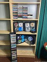 Full view of shelf holding many stacked CDs and three CD wallets with multiple discs inside, plus a standing CD storage tower full of CDs.