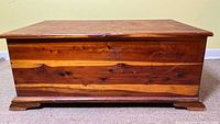 Full front view of the wooden cedar chest showing scratches and watermarks on the front panel, along with the wooden base.