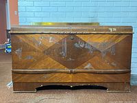 Front view of cedar chest with geometric veneer, scratches, and wear on wood surface.