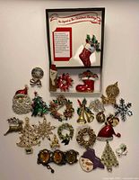 Top view of the majority of Christmas brooches laid out showing various styles including Santa, trees, wreaths, stockings, and snowflakes