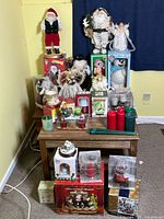 Full view of lot with Christmas figurines, angels, Santa Claus, assorted candles and boxed decorations on a wooden table and the floor