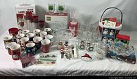 Wide shot of assorted Christmas glassware, mugs, serving dishes, salt and pepper shakers, and holiday decor items displayed on a table.