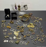 Wide photo showing the entire lot including numerous earrings and three bangles arranged on a black surface.