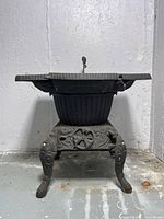 Front view of Daisy wood or coal-burning stove showing ornate cast iron base and legs with detailed design.