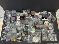 Top-down view of a large assortment of costume earrings in multiple plastic bags, arranged on a black surface showing diverse shapes and colors.