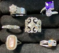 Seven rings displayed on black velvet with mixed silver and gold tones with various gemstones