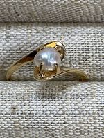 Angled view of ring on fabric background showing white freshwater pearl set in gold band
