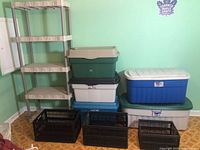 Full view of beige plastic shelving unit and stacked Rubbermaid totes in various sizes and colors with 3 collapsible black boxes at front