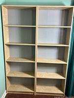 Full view of the pair of IKEA bookshelves side by side against a wall with teal curtains nearby.