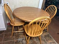 Photo showing three wooden spindle back chairs positioned around a round wood dining table.