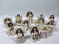 Group of 16 Kneeded Angel figurines displayed on white background with varied hair colors and some holding flowers or small objects.