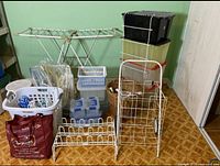 Group of laundry and storage items displayed against a green wall and wooden floor including drying rack, plastic baskets, wicker baskets, rack, totes, and laundry cart
