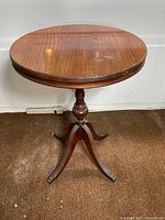 Full view of circular mahogany pedestal side table with tripod base showing brass claw feet and visible wear on base and tabletop.