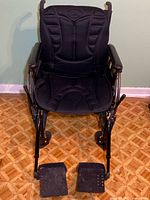 Front view of wheelchair with black padded back massager cushion, armrests, footrests, and large rear wheels.