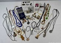 Overview of all jewelry items laid out on white surface including necklaces, earrings, brooches, and pendants showing size, color, material variety.