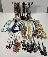 Photo showing assortment of colorful beaded necklaces spread on table with some matching earrings visible, in various colors including orange, black, green, blue, white, and more