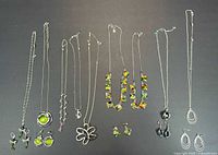 Full overview of assorted necklaces and earrings arranged side by side on black background showing color, style and metal finish details.