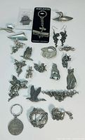 Photo showing all pewter brooches, keychains, and earrings arranged on white background. Includes airplane keychain on Sparta Pewter card.