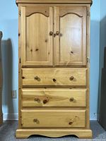 Front view of pine armoire showing natural wood tone, 3 drawers with knobs, and two paneled doors above drawers.