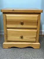 Front view of pine side table showing two drawers with wooden knobs and base detail.