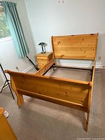 Pine sleigh bed frame assembled in room showing headboard, footboard, side rails, and metal support frame undercarriage