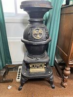 Front view of the cast iron pot belly stove showing the circular door with a brass wheel and a brass vent panel below it, standing on four curved legs.
