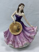 Front view of Royal Doulton figurine showing the woman in a purple and pink dress holding a straw hat with roses.
