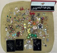 Full top-down view of assorted holiday/seasonal jewellery including earrings, bracelets, pins, and a necklace arranged on cloth