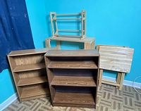 Lot contents including brown bookcase, wooden slat shelf, and folding TV trays placed against wall.