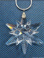 Close-up front image of clear Swarovski star pendant on silver chain against textured blue background.